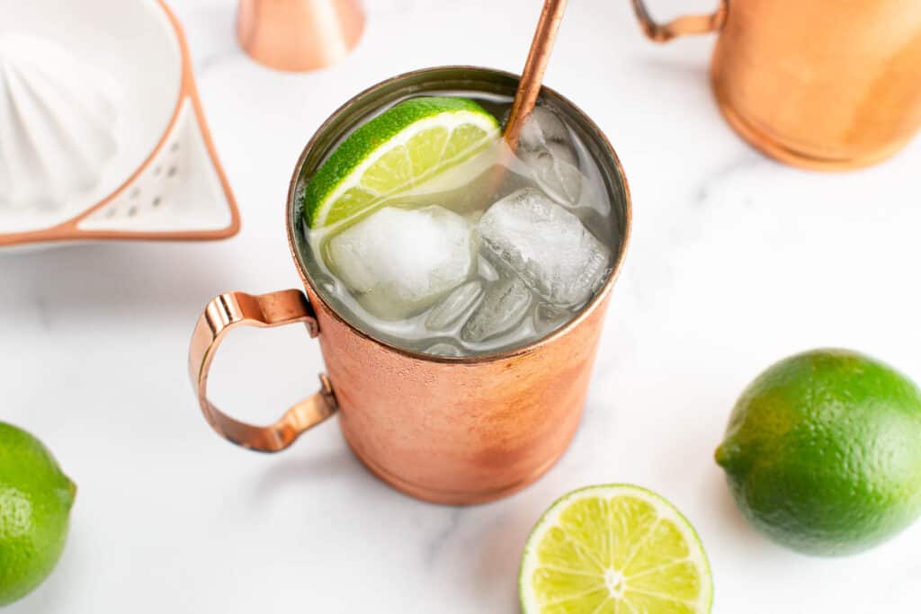 A Moscow mule with limes and a juicer on a marble background. 