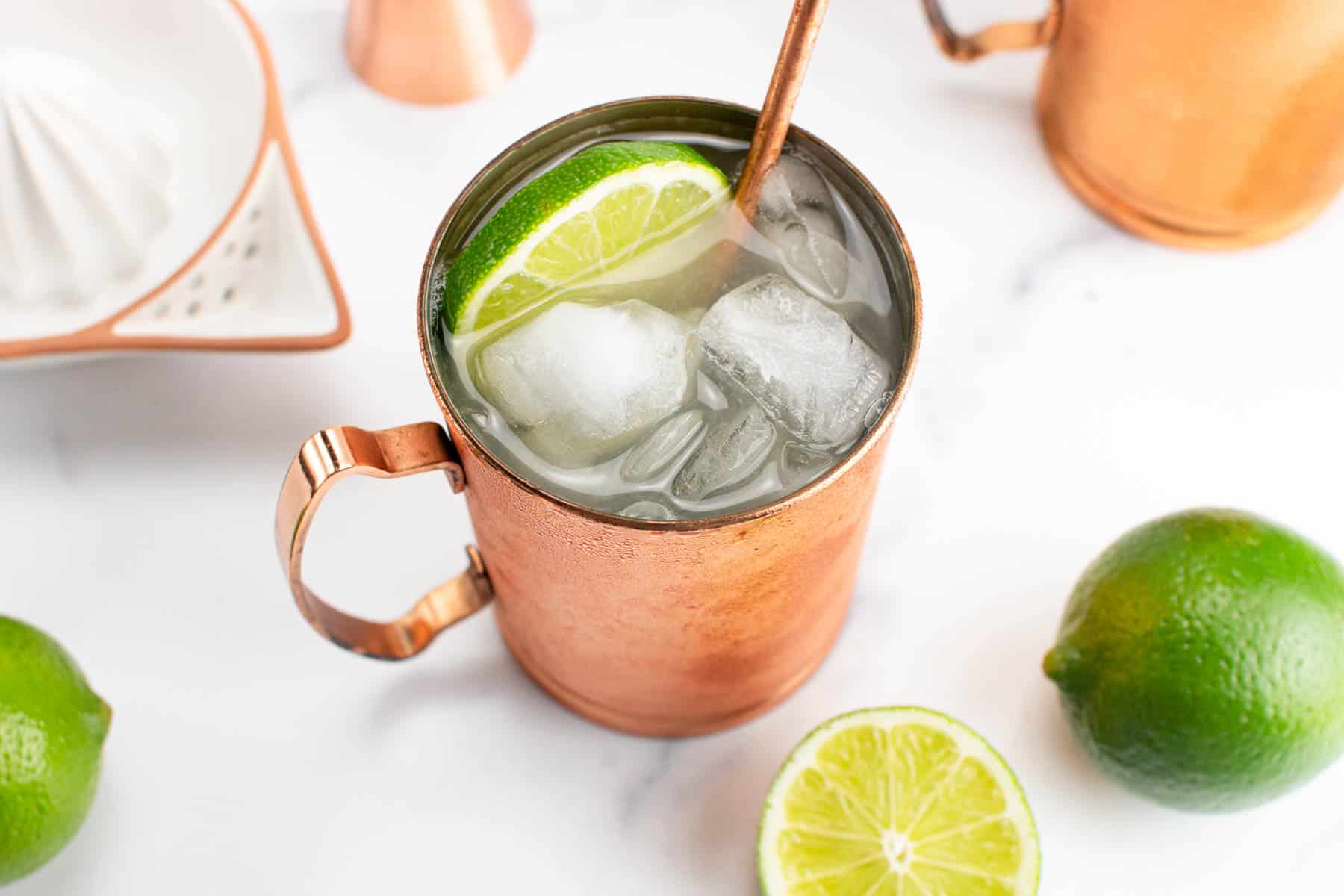 A Moscow mule with limes and a juicer on a marble background.