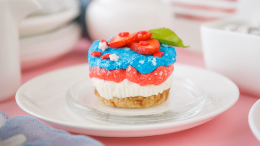 Red, white and blue mini cheesecakes decorated with strawberries on a white plate.