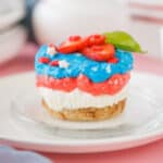 Red, white and blue mini cheesecakes decorated with strawberries on a white plate.