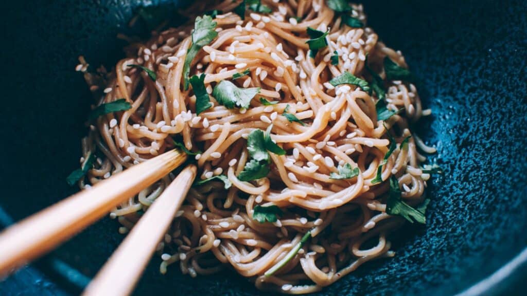 Chopsticks sticking out of a black bowl of sesame noodles.