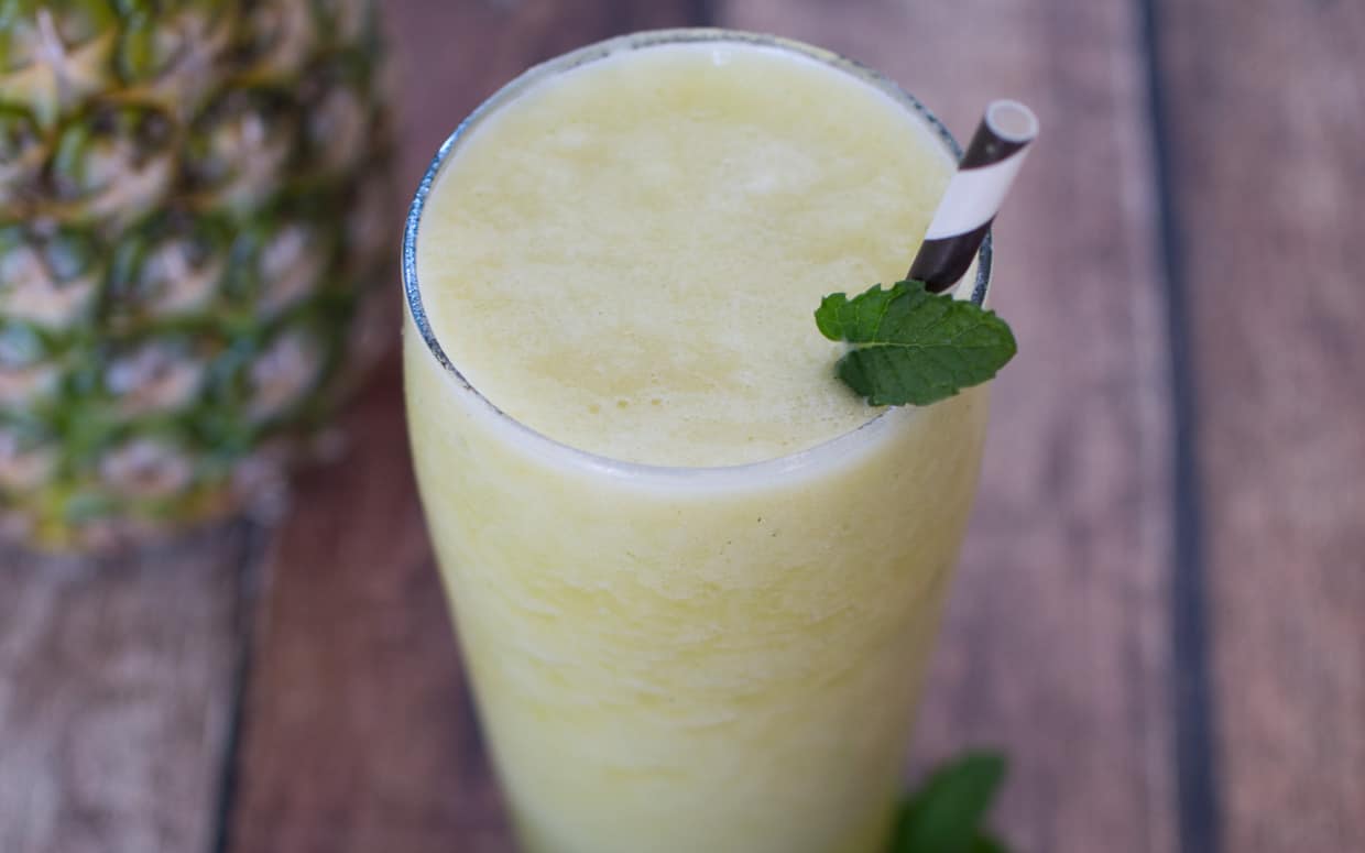 Closeup of pineapple smoothie with sprig of mint and a pineapple.