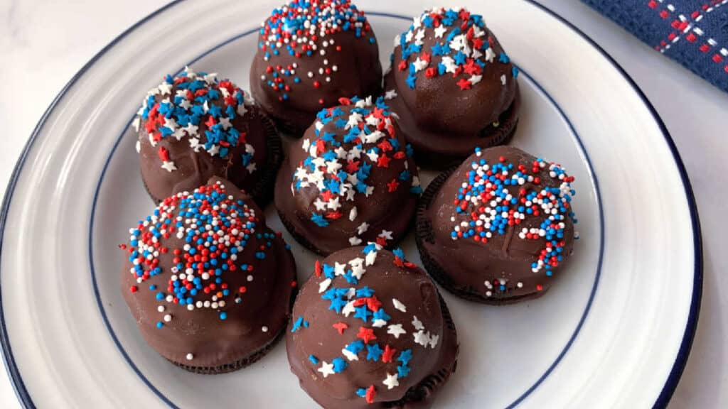 Chocolate covered ice cream bites with red, white and blue sprinkles on a white plate.