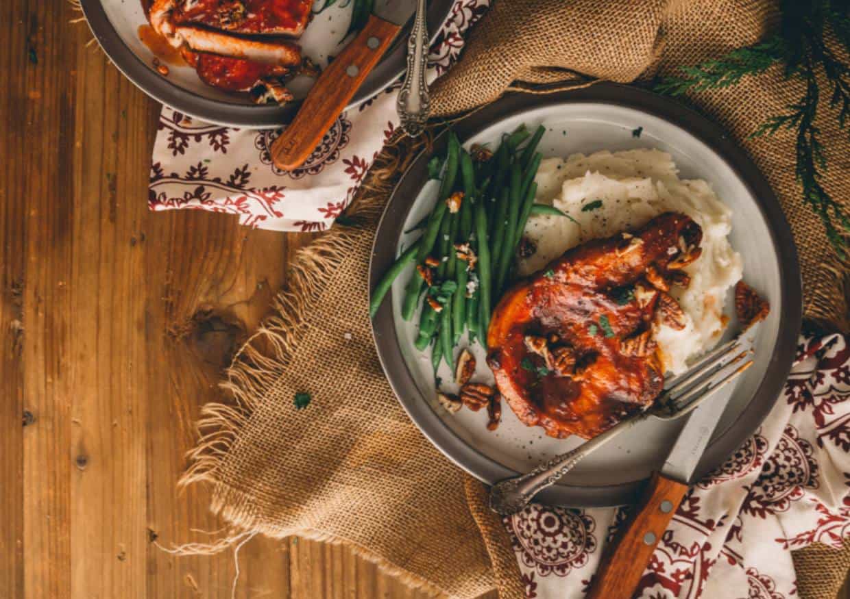 Baked bbq pork chop on dinner plate with mashed potatoes and green beans.