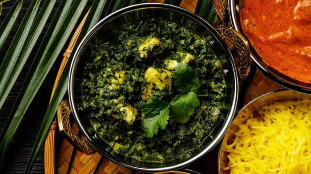 Overhead shot of palak paneer with rice and palm fronds on the side.