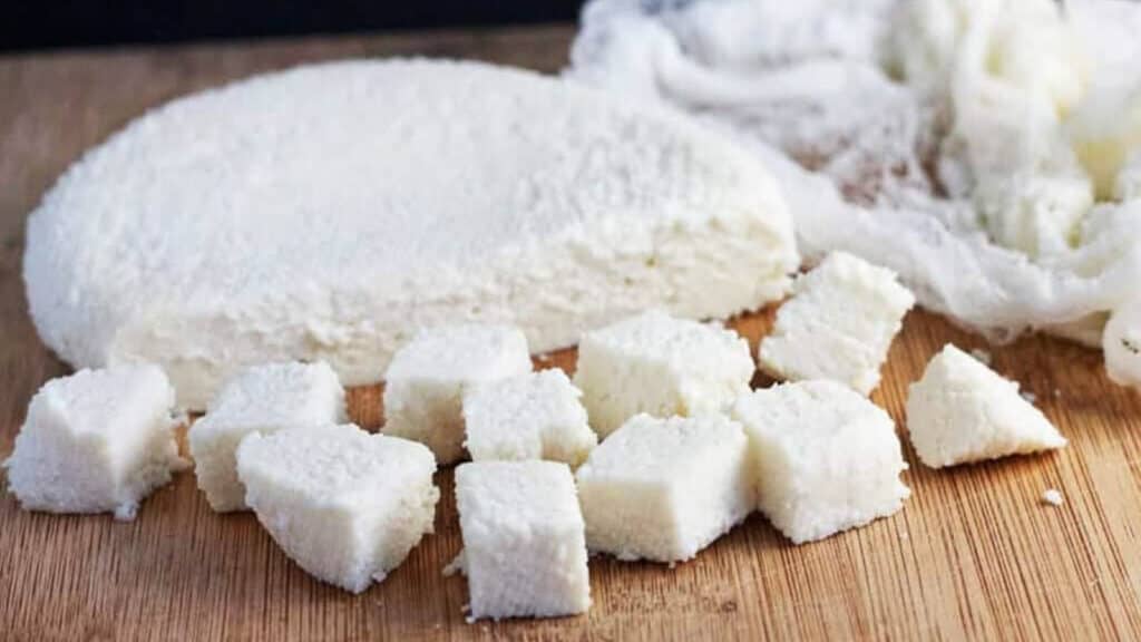 Homemade paneer, cubed, on a cutting board.