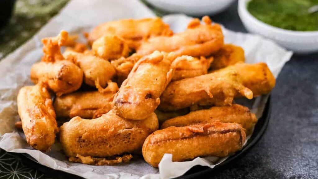 low angle shot of a pile of paneer pakora on a parchment lined plate with dipping sauces in the background.