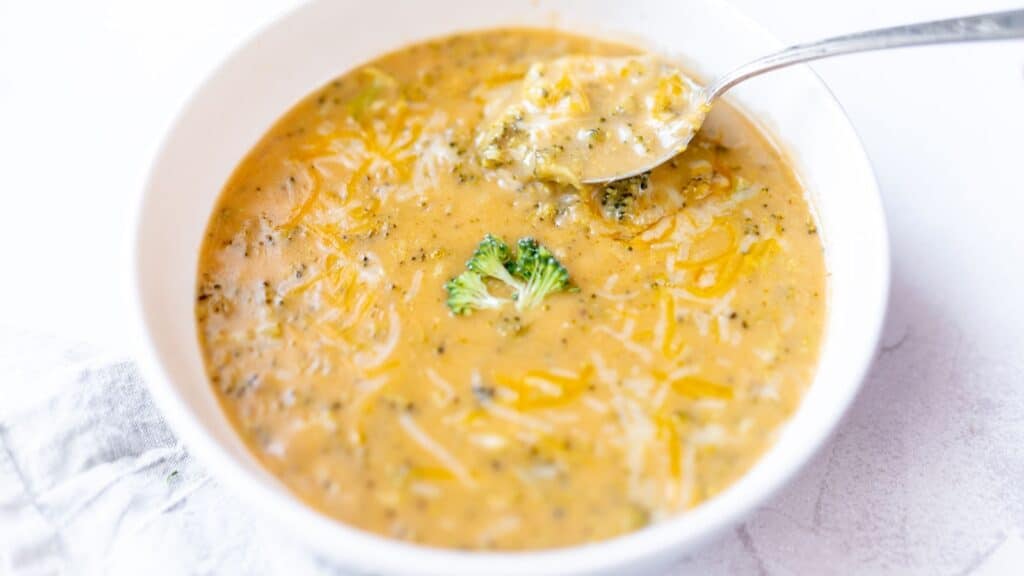 A silver spoon dips into a white bowl filled with a cheesy soup.