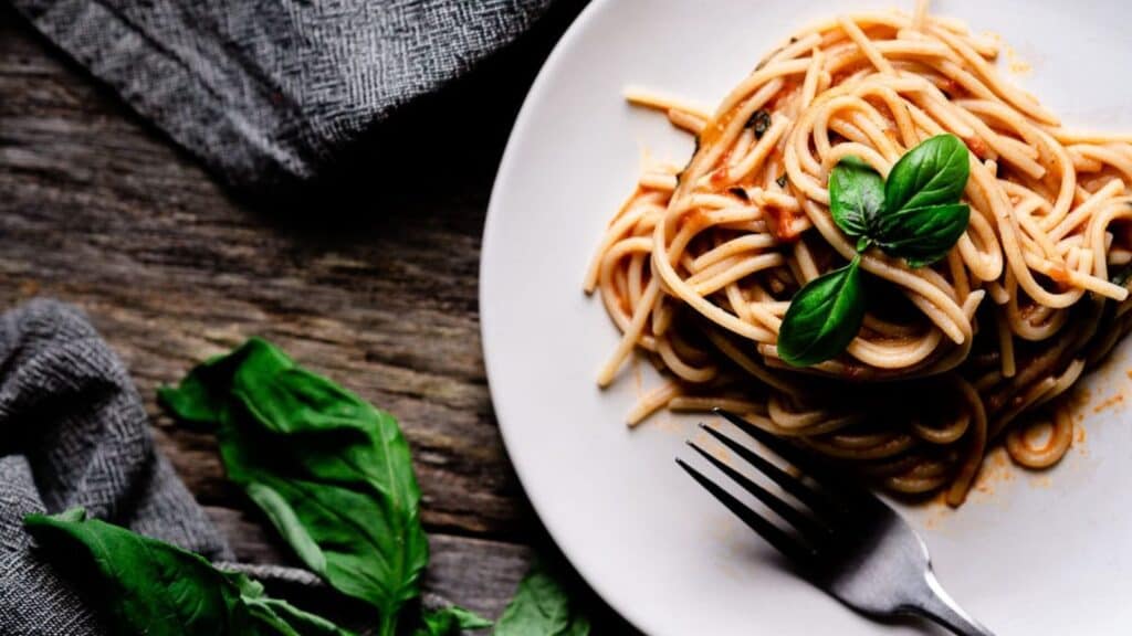 Spaghetti resting on a white plate on a wooden table.