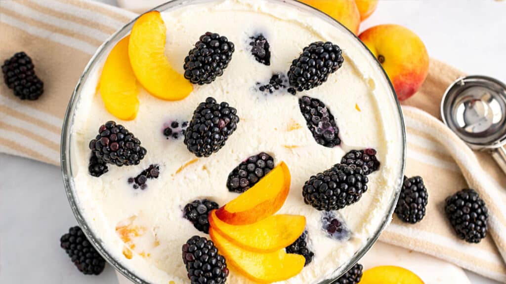 A bowl of peach ice cream with blackberries.