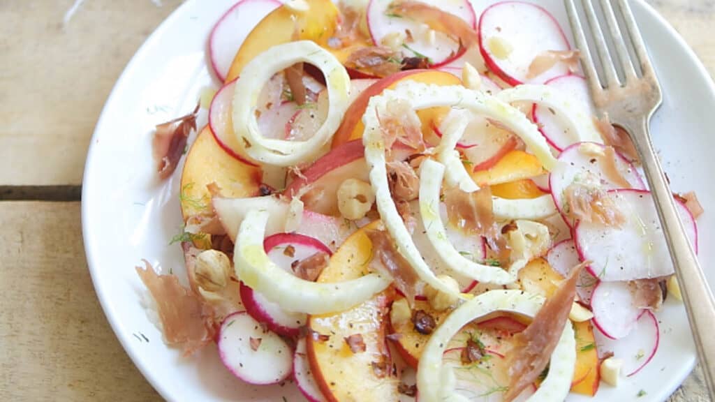 Peach radish salad with crispy prosciutto on a white plate with a fork.
