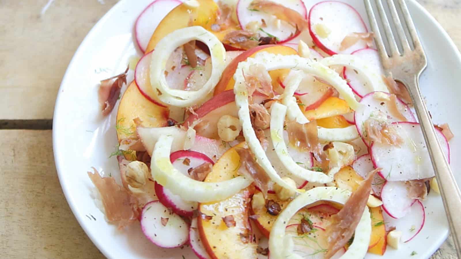 Peach radish salad with crispy prosciutto on a white plate with a fork.