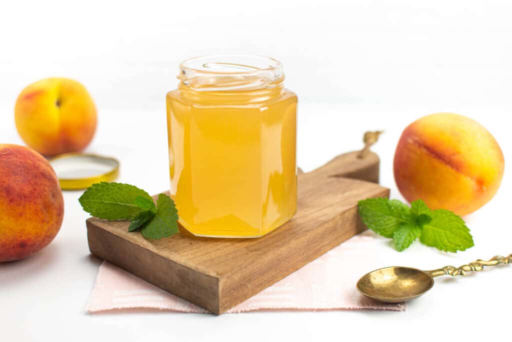 Peach syrup in a hexagonal jar on top of a wood board. 