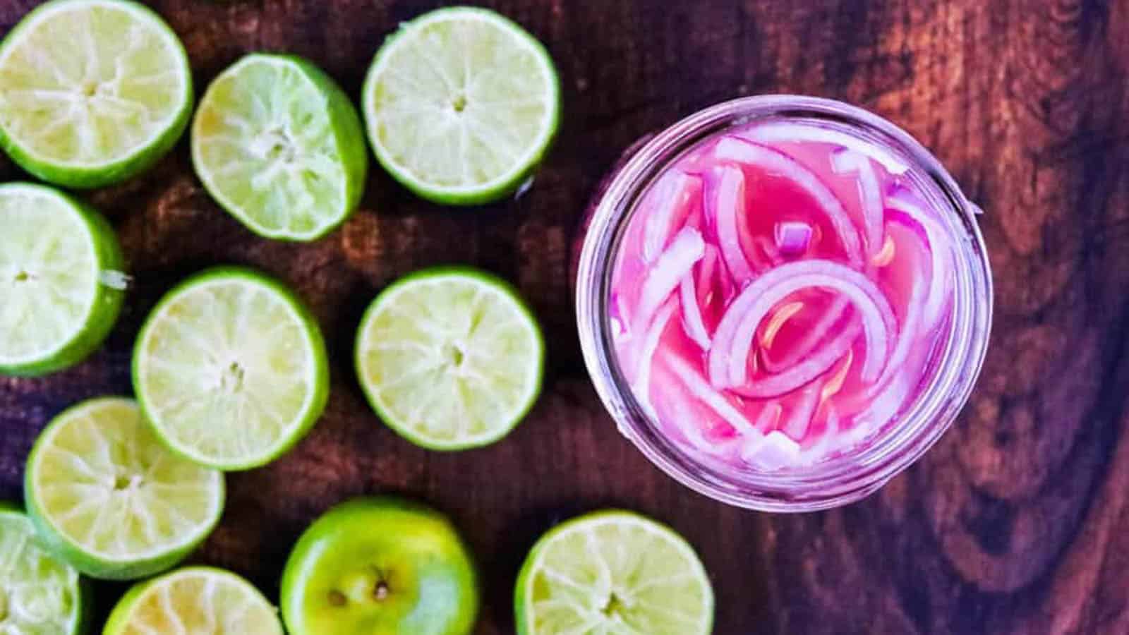 Overhead shot of a jar of pink pickled onions with lime halves on the side.