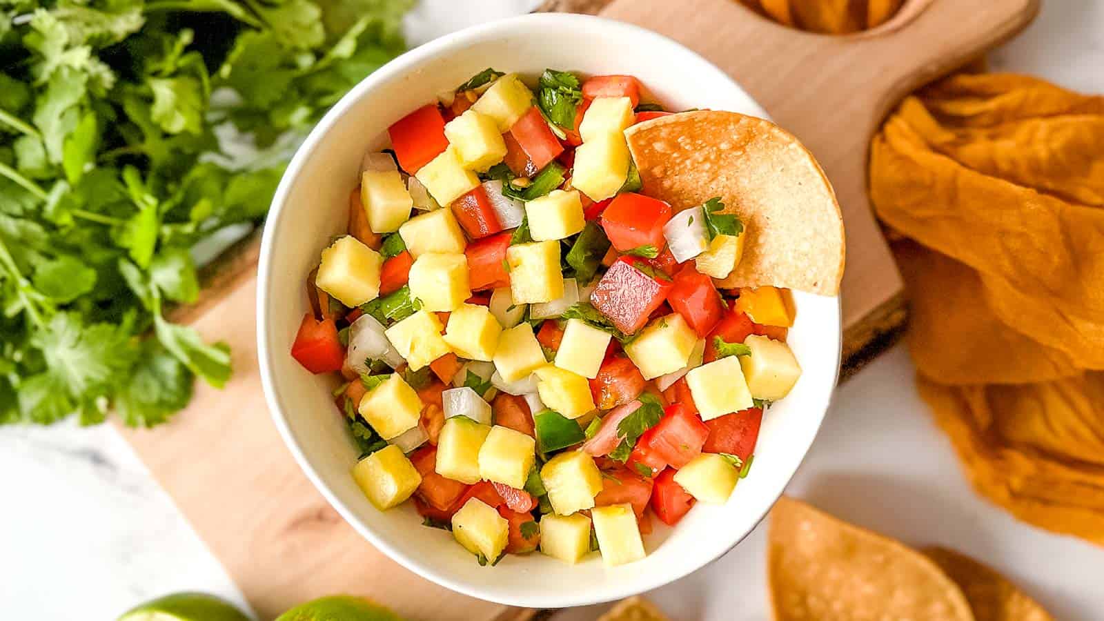 Pineapple pico de gallo in a black bowl surrounded by limes and a yellow linen.