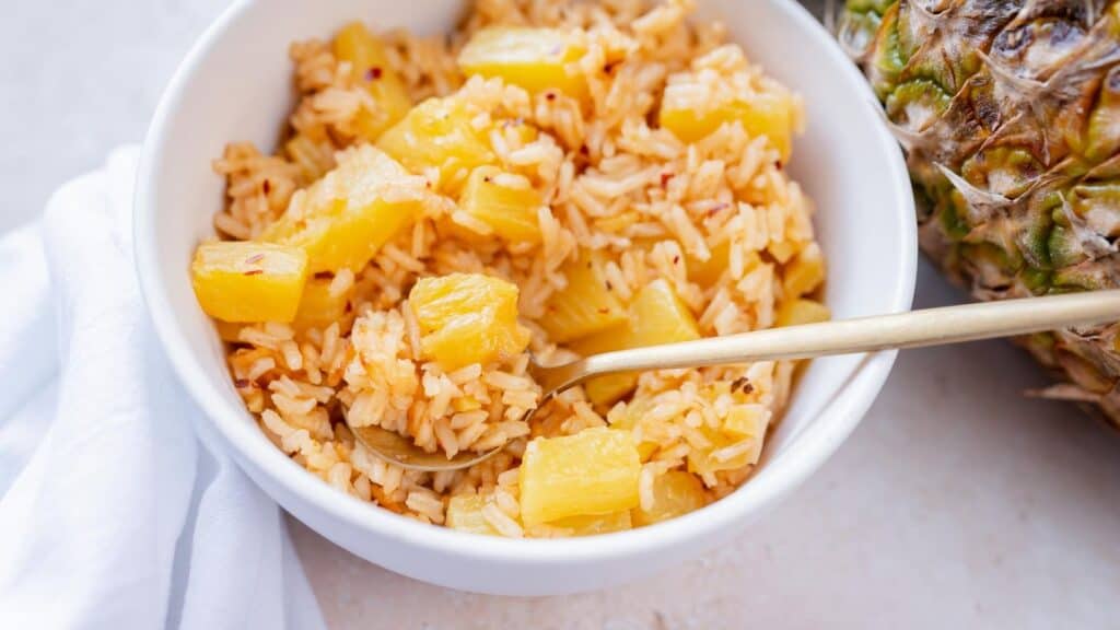 A small white ceramic bowl of rice with pineapple in it.