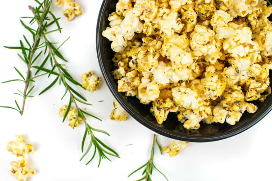 Pizza popcorn in a bowl with fresh rosemary.