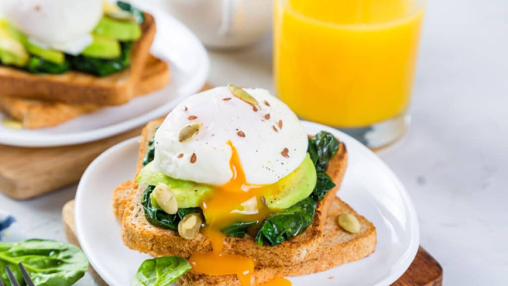 Low angle shot of a poached egg with yolk running out over toast that is topped with greens and avocado.