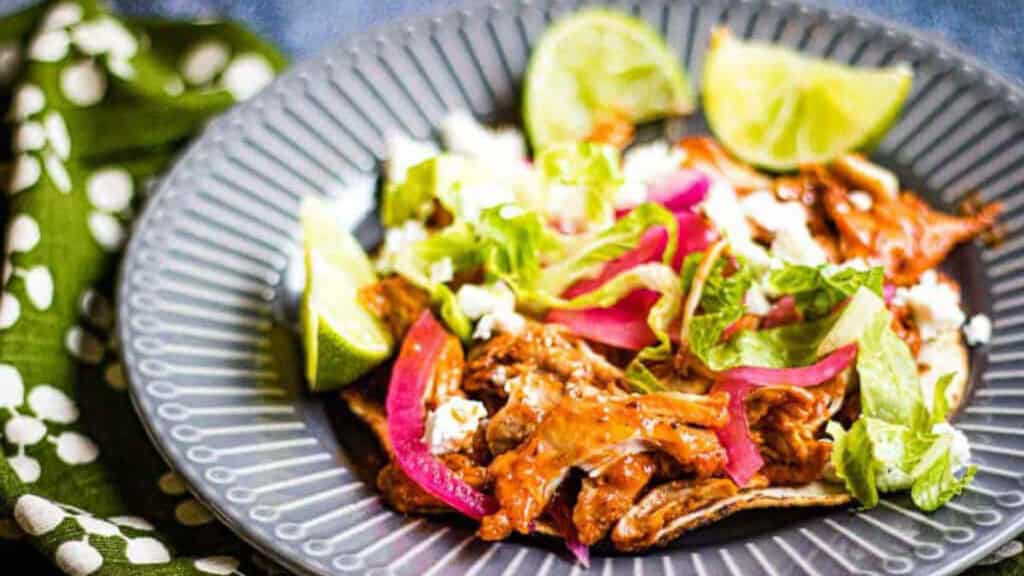 Pollo pibil on a grey plate with limes and shredded lettuce.