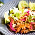 Pollo pibil on a grey plate with limes and shredded lettuce.