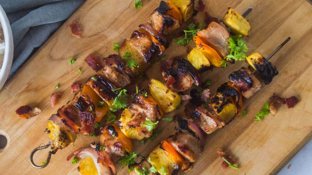 Three pork kabobs with pineapple on a wooden cutting board.