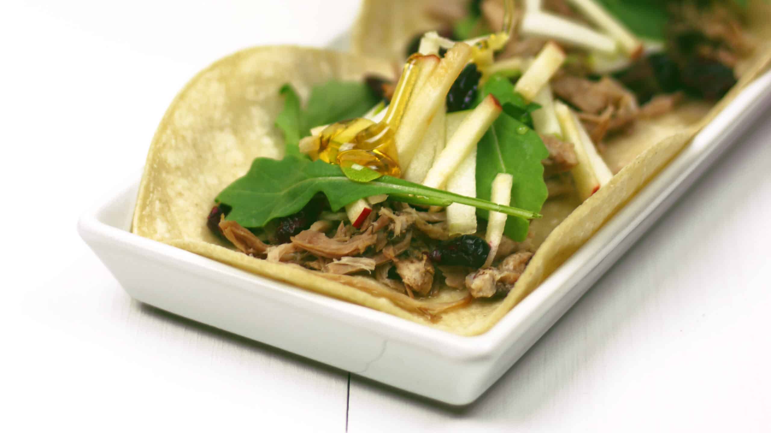 A white tray of apple cider pulled pork tacos.