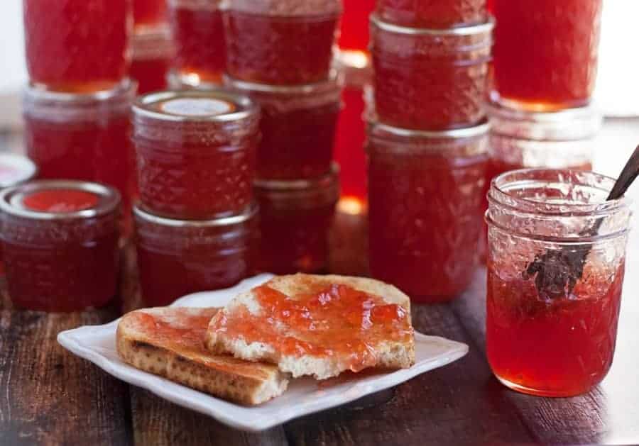 Jars of quince jelly and a piece of toast on a plate with quince jelly spread on top.