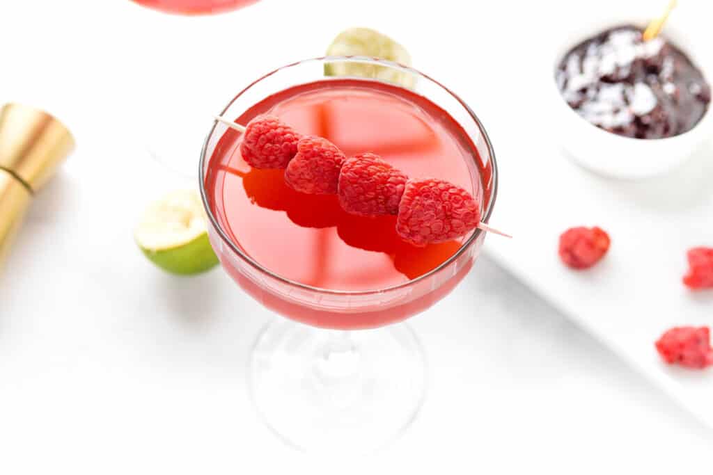 Raspberries garnish a cocktail in a stemmed glass.