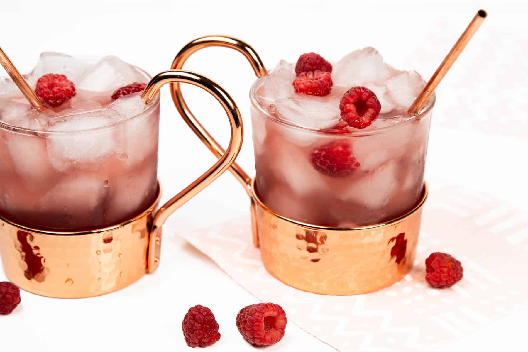 two raspberry Moscow mules in glass and copper mugs.