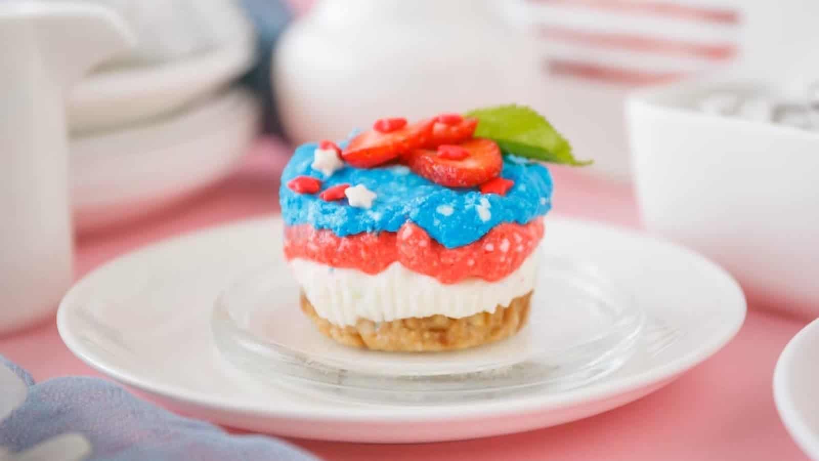 A red, white and blue mini cheesecake on a mini glass and white ceramic plates.