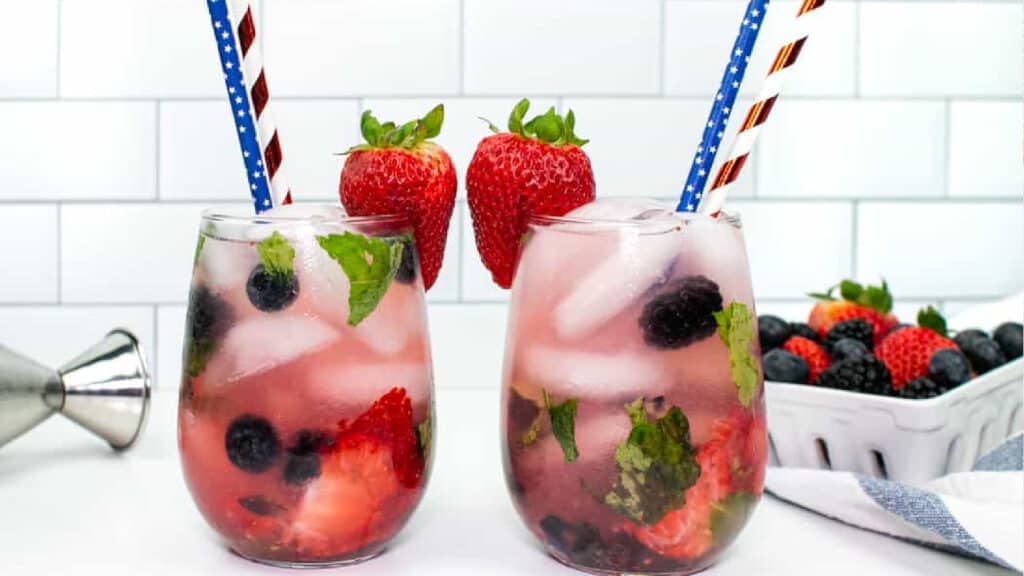 Two red white and blue mojitos garnished with strawberries and patriotic straws.