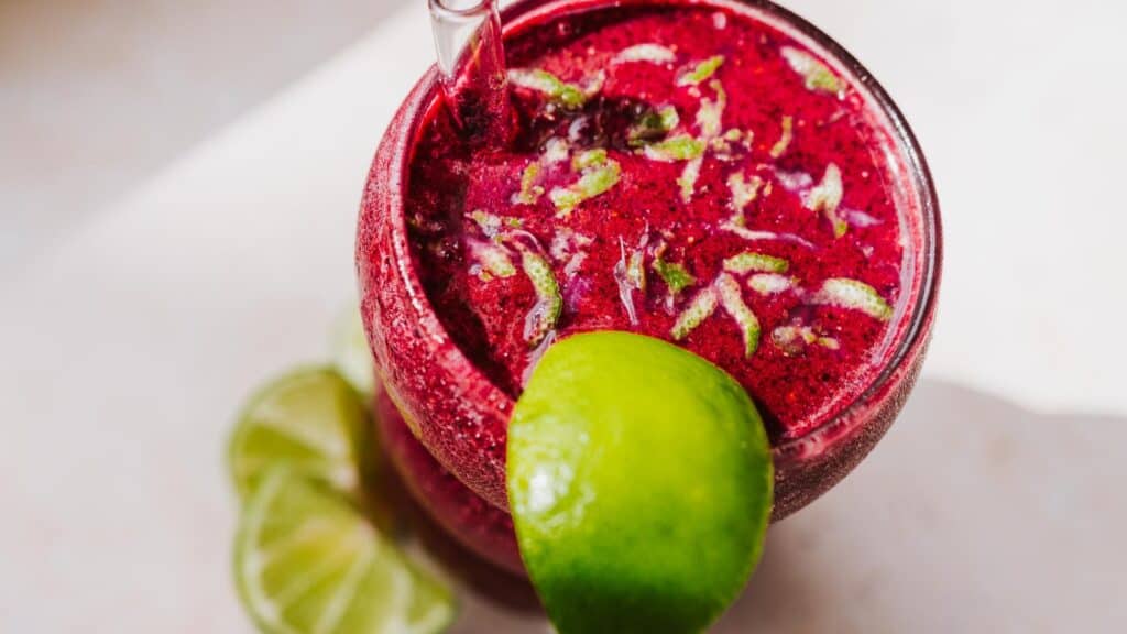 A close shot of a purple drink garnished with lime zest.