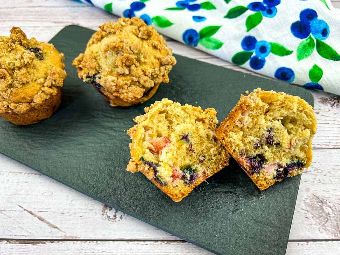 Blueberry Rhubarb Muffins on a black plate with one muffin cut in half.