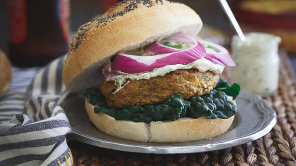 Roasted eggplant curry burger on a bun with kale, red onions and cilantro hummus sauce.