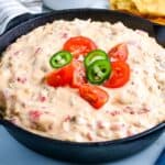 Sausage cheese dip in a cast iron skillet topped with tomatoes and jalapenos.