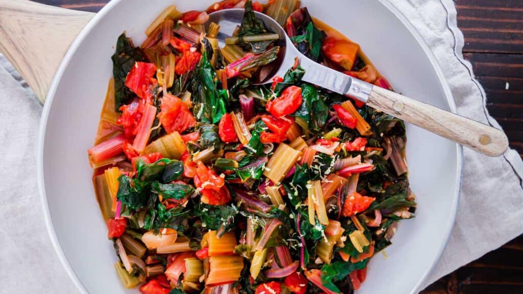 Sautéed Swiss chard in a white skillet with wooden serving spoon.