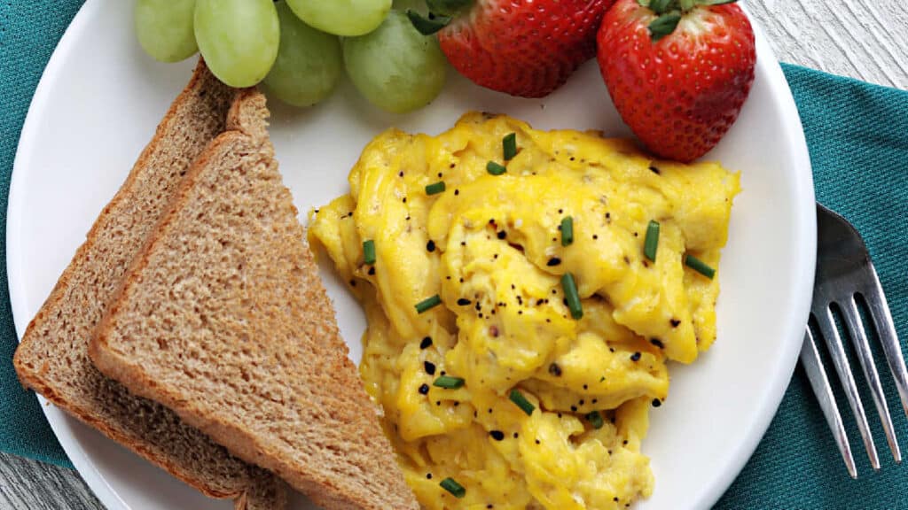 A white plate with scrambled eggs and toast.