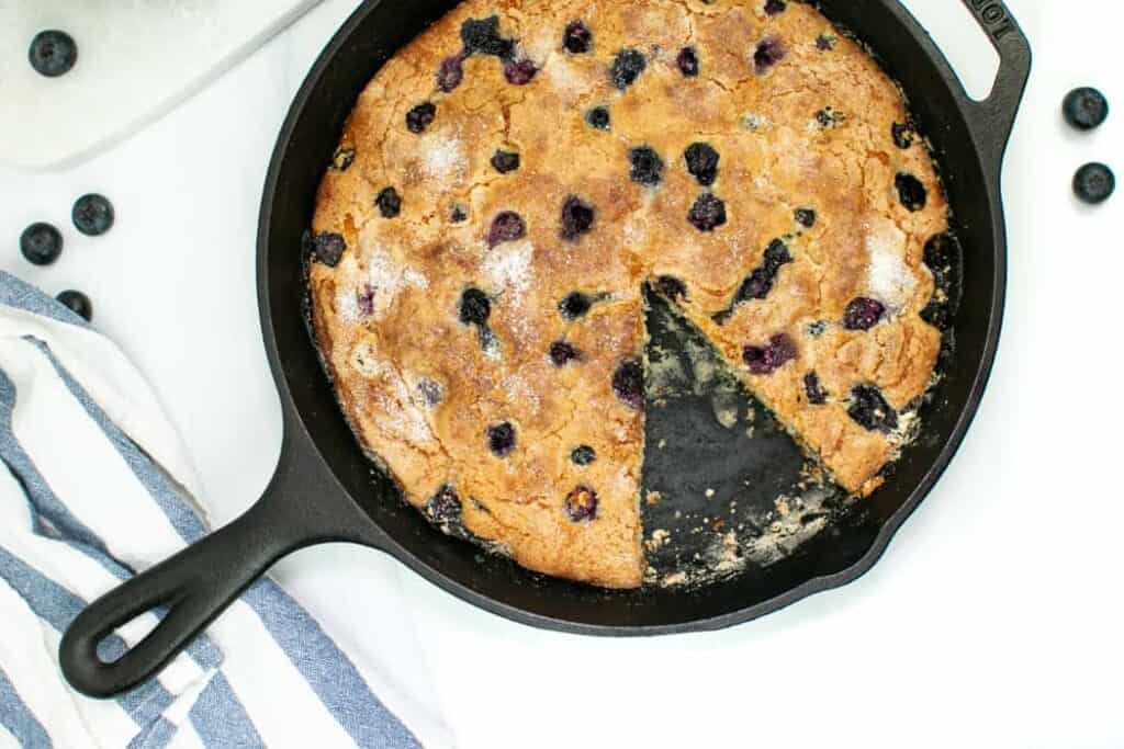 Skillet Blueberry Coffee Cake in.a cast iron skillet with a blue and white striped kitchen towel.