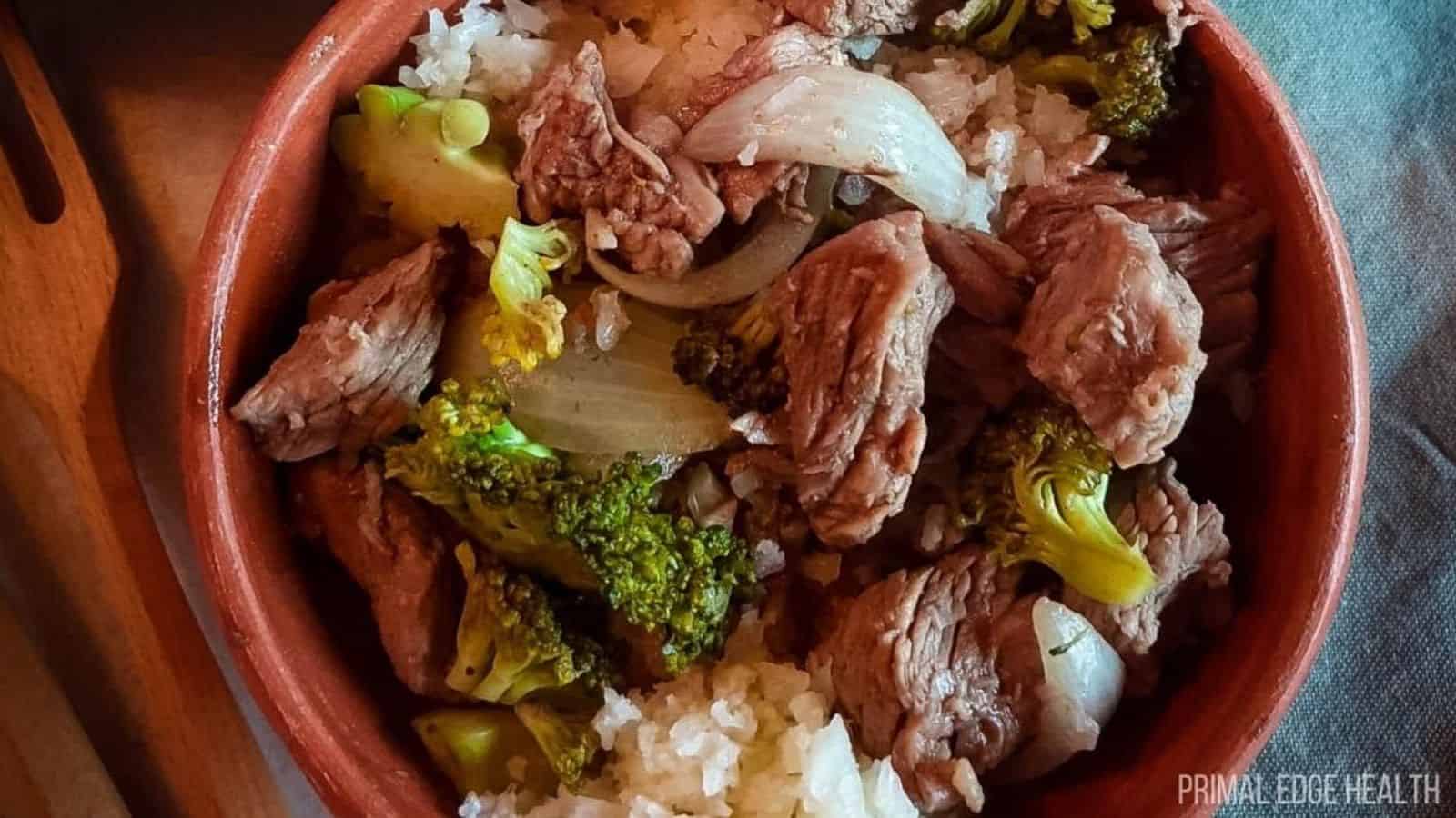 Slow cooker beef and broccoli with onion in brown bowl.