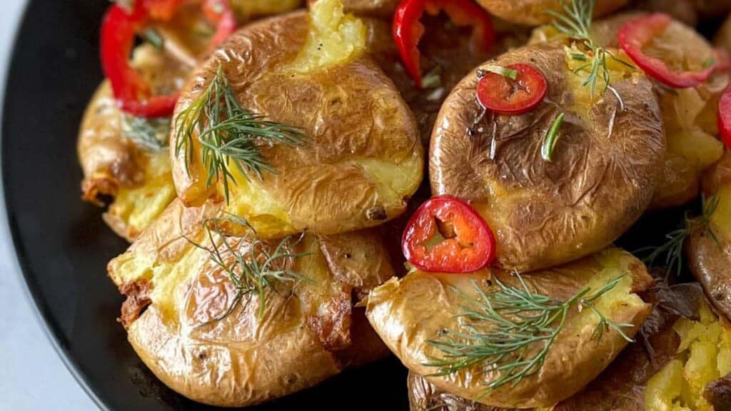 Smashed potatoes with dill on a black plate.