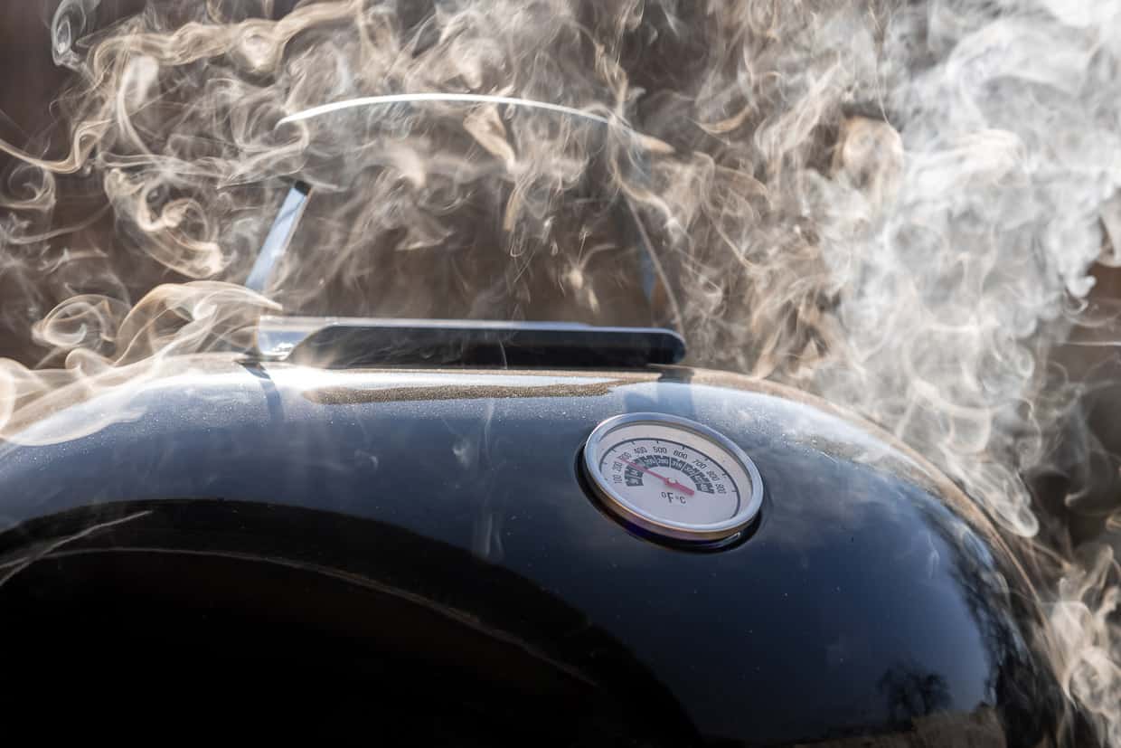 The lid of a pellet smoker with smoke coming out of it.