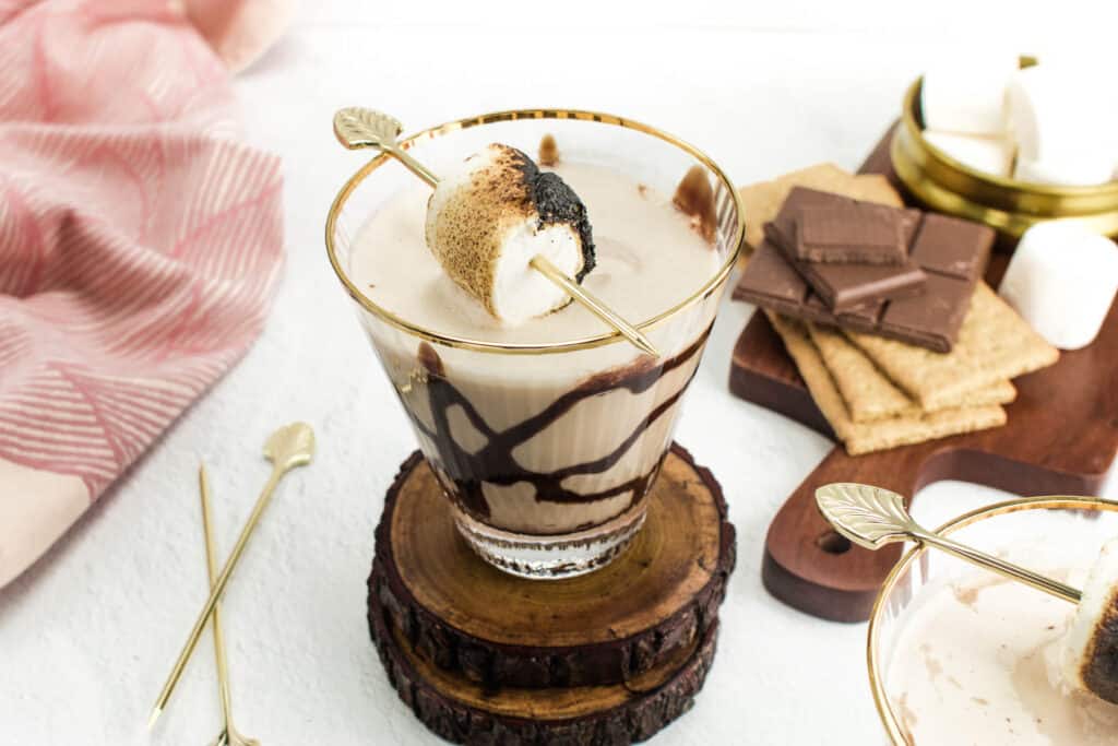 A wooden cutting board holds s'more ingredients next to a martini.