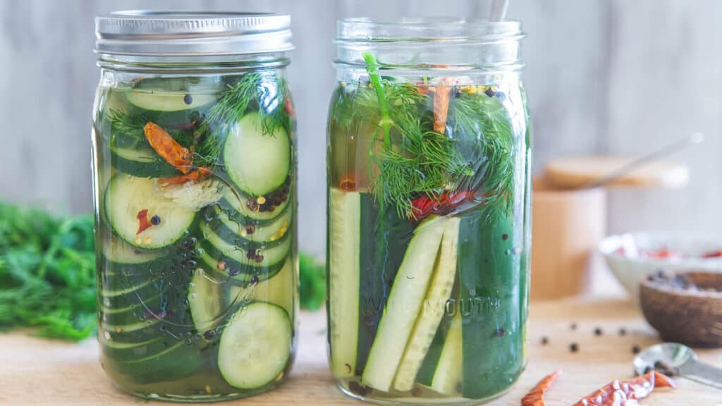 Spicy garlic dill pickles in mason jars on a wooden surface.