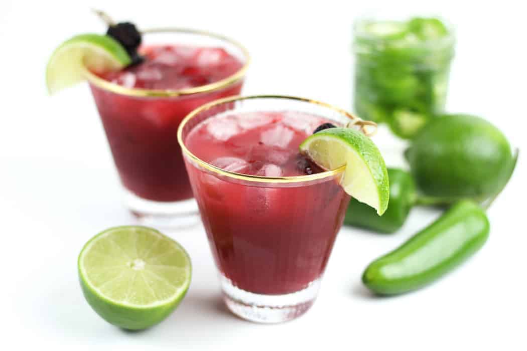 two red margaritas made with jalapeño tequila with limes and blackberries.