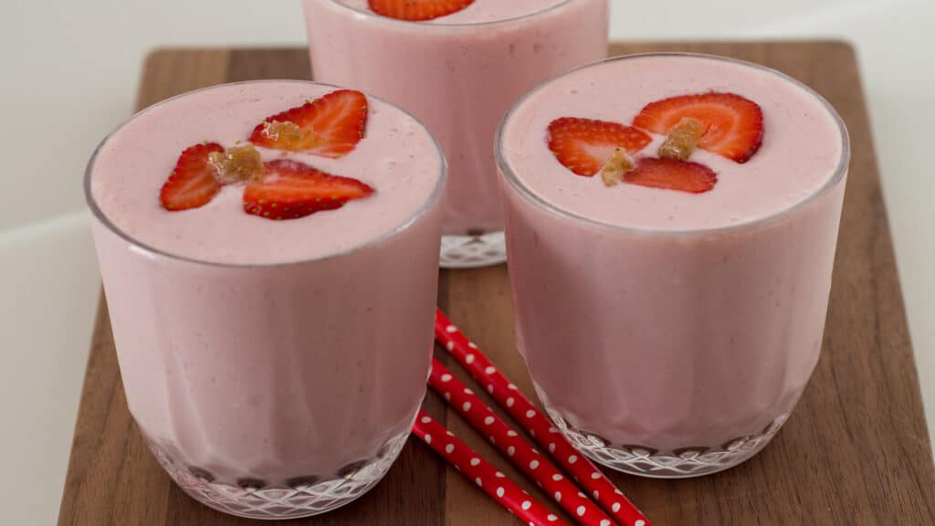 Two glasses of strawberry smoothie on a cutting board.