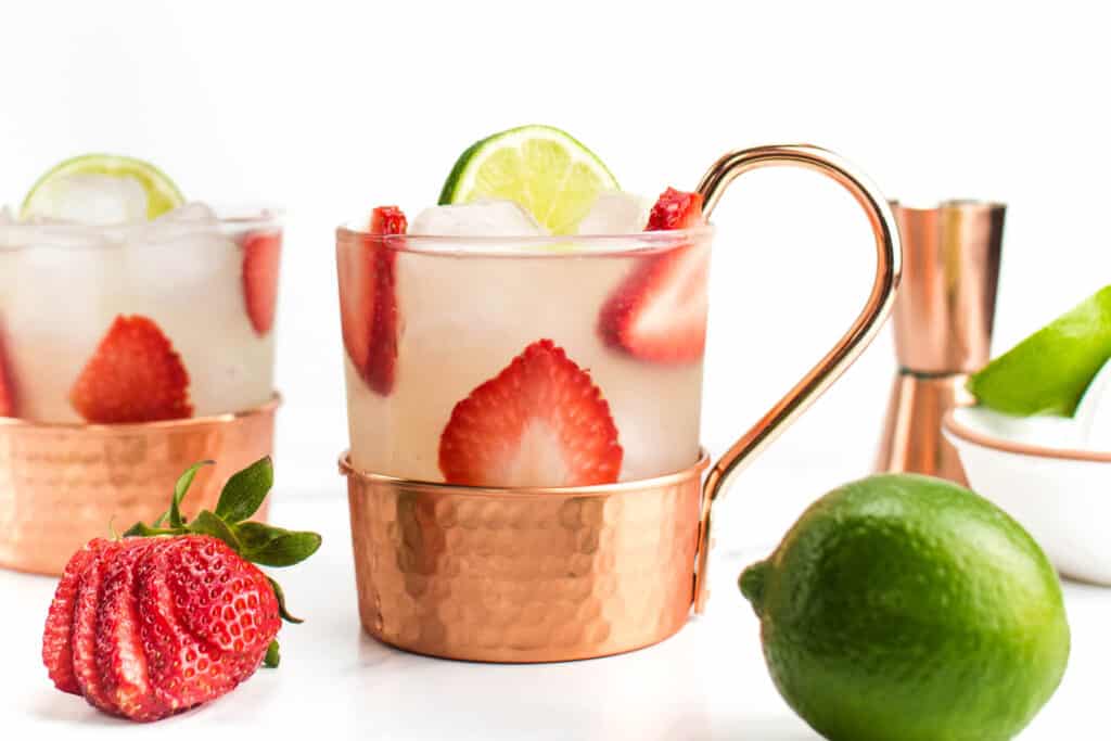 Two strawberry mules next to a sliced strawberry and whole lime.