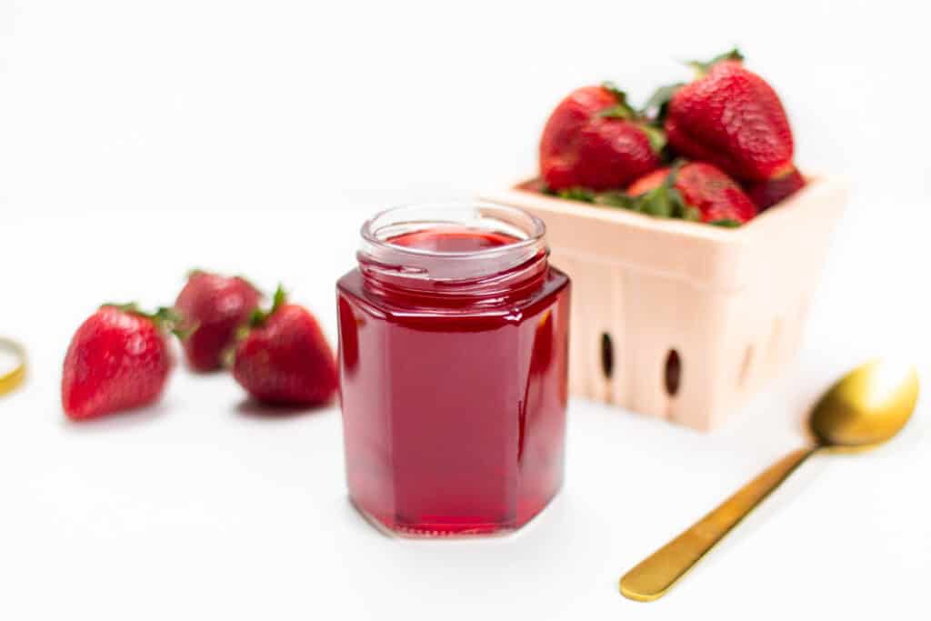 a jar of strawberry simple syrup with fresh berries and a gold spoon.