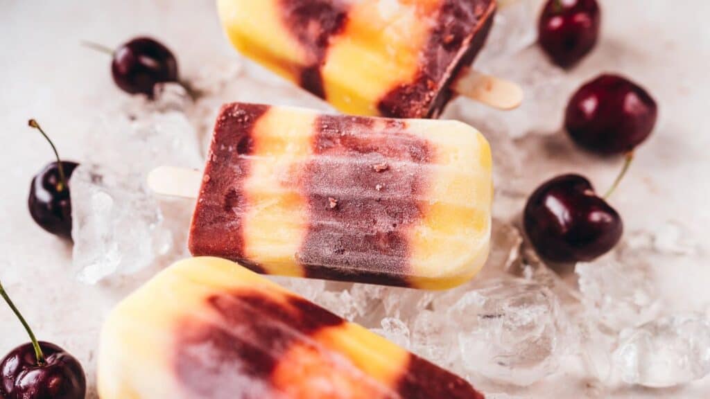 Cherry mango popsicles resting on ice cubes.