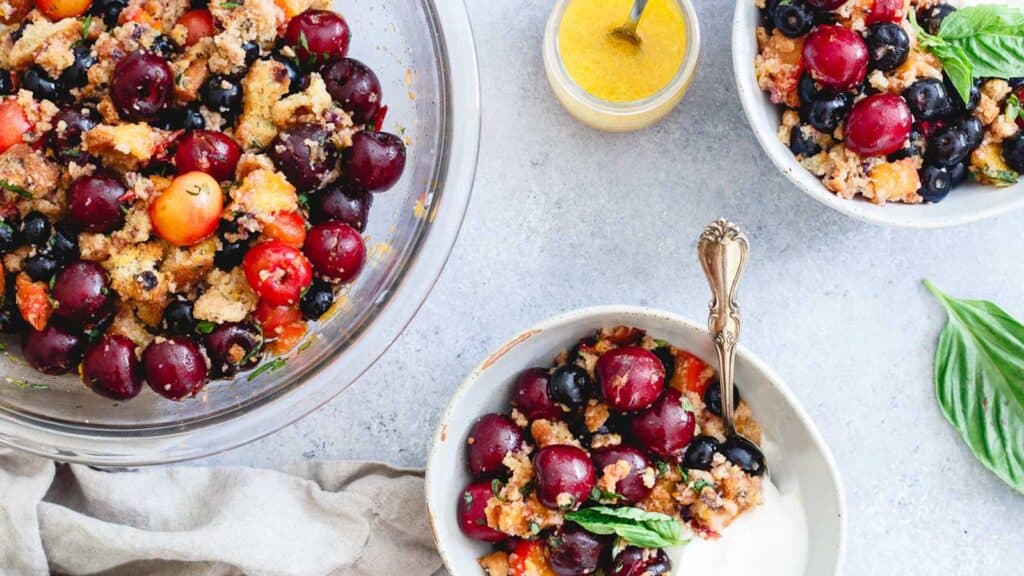 Summer fruit panzanella salad in a glass bowl with smaller bowls on the side.