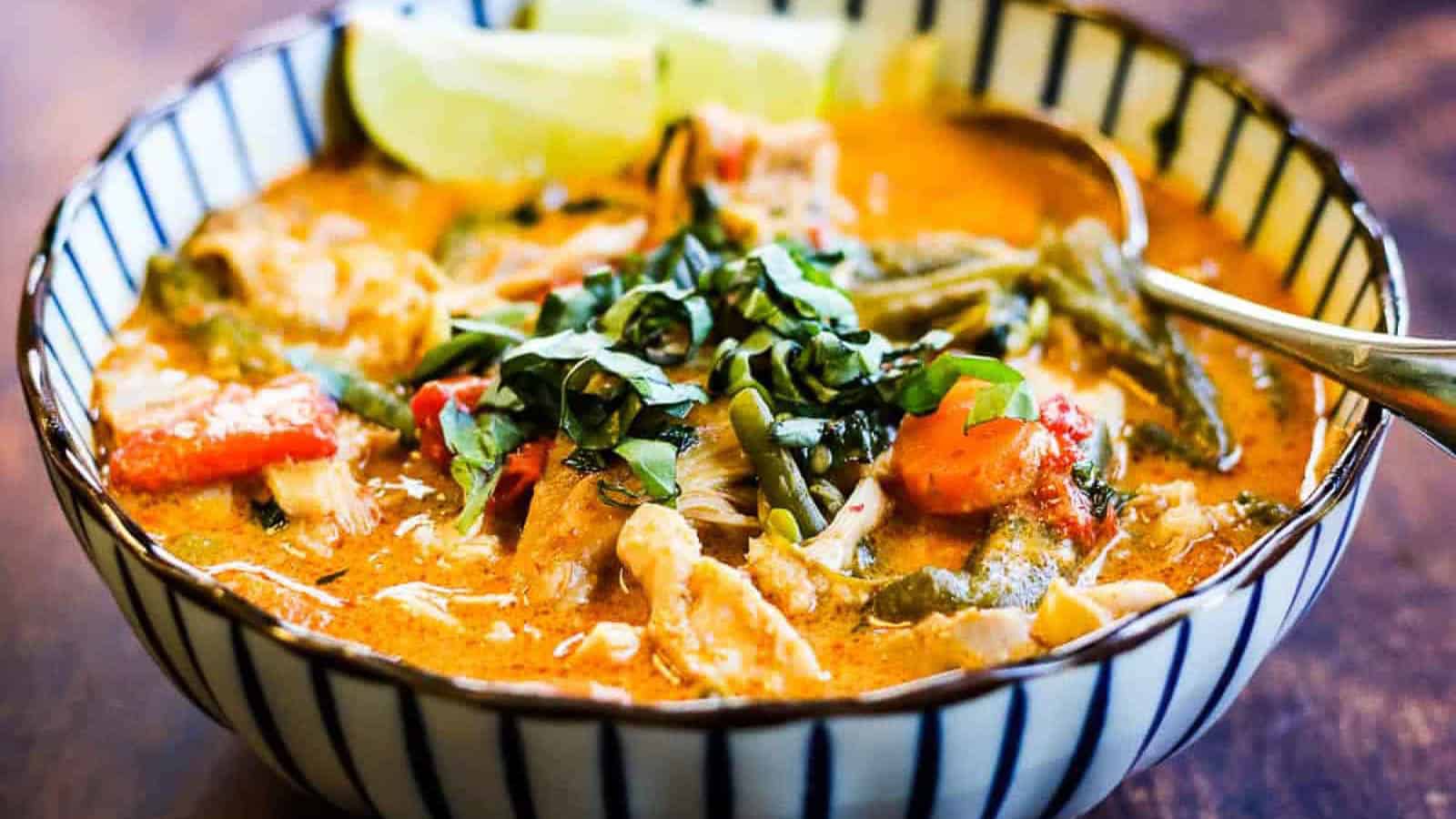 Thai chicken curry in a striped bowl with basil and lime wedges.